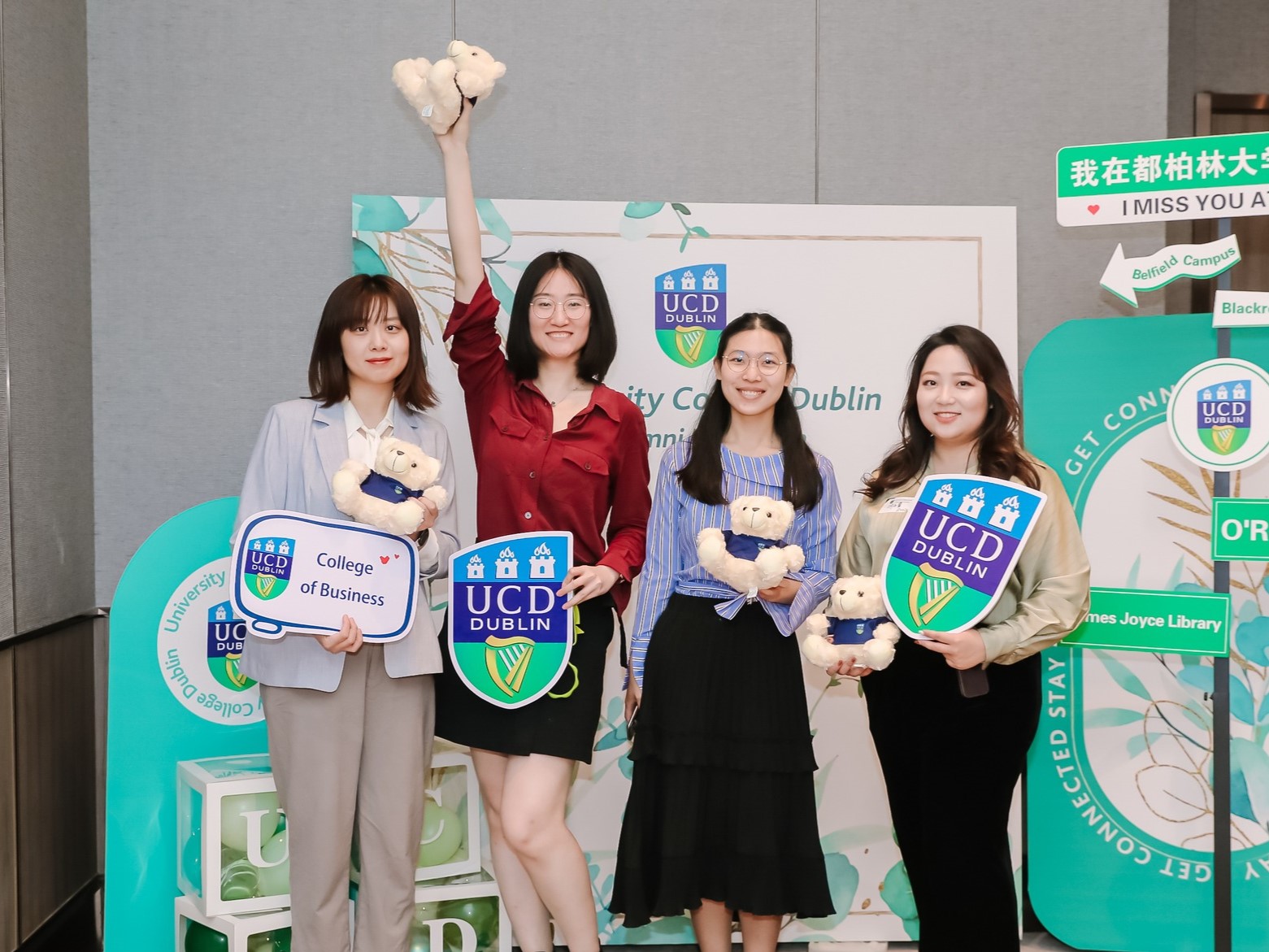 Four alumni posing with UCD signs and memorabilia.