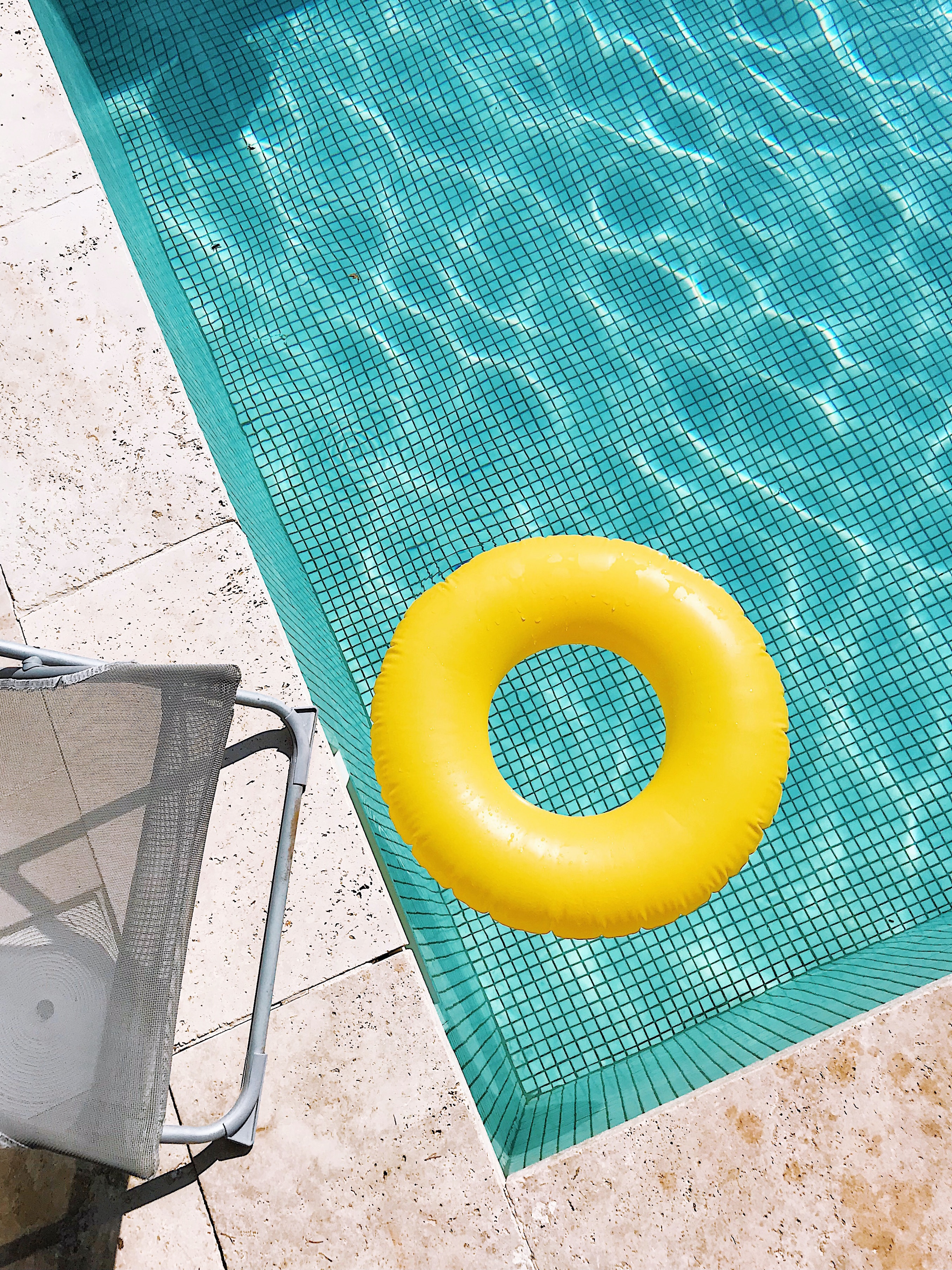 Image of a pool with a deckchair on the left and a yellow ring floating in the pool