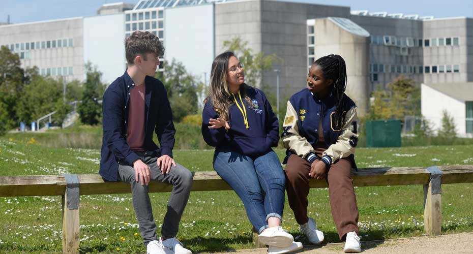 Three students sitting on front of the College of Engineering