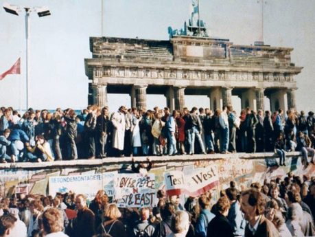 People with signs on the Berlin wall in front of the Brandenburg Gate in 1989