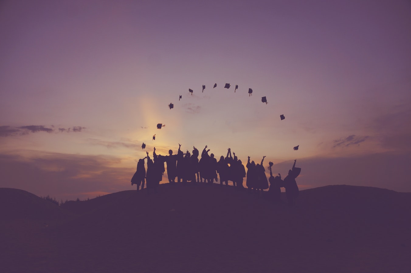 Students throwing their caps in the air set to a sunset background