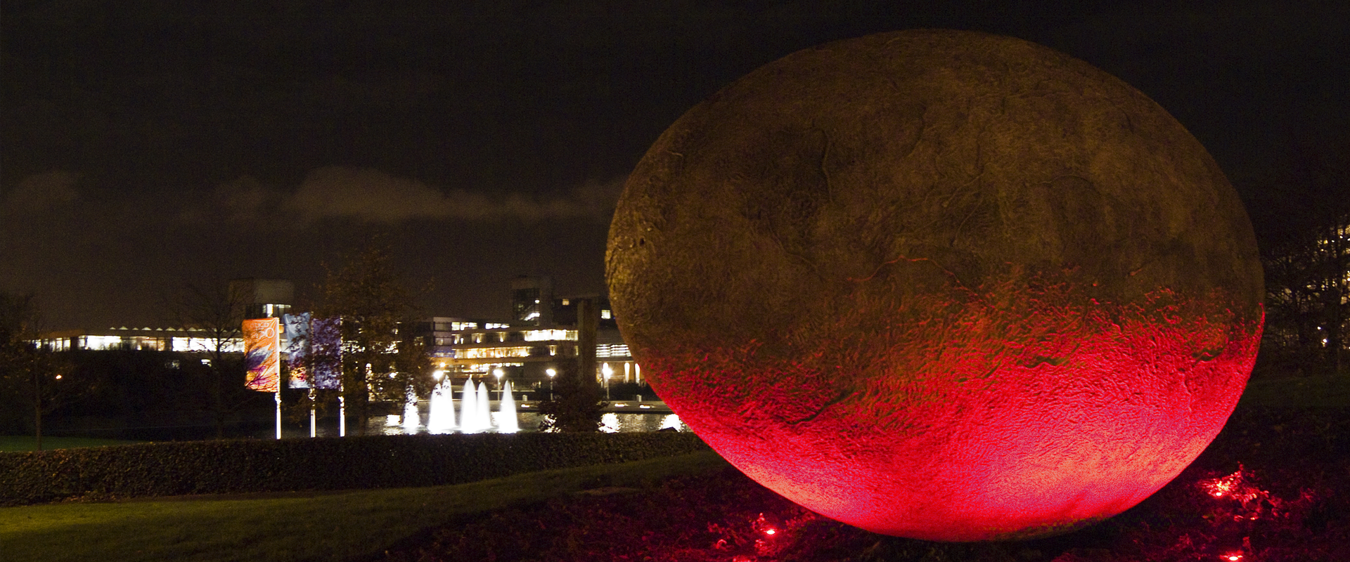 Sculpture at night with the lake and fountains in the background.