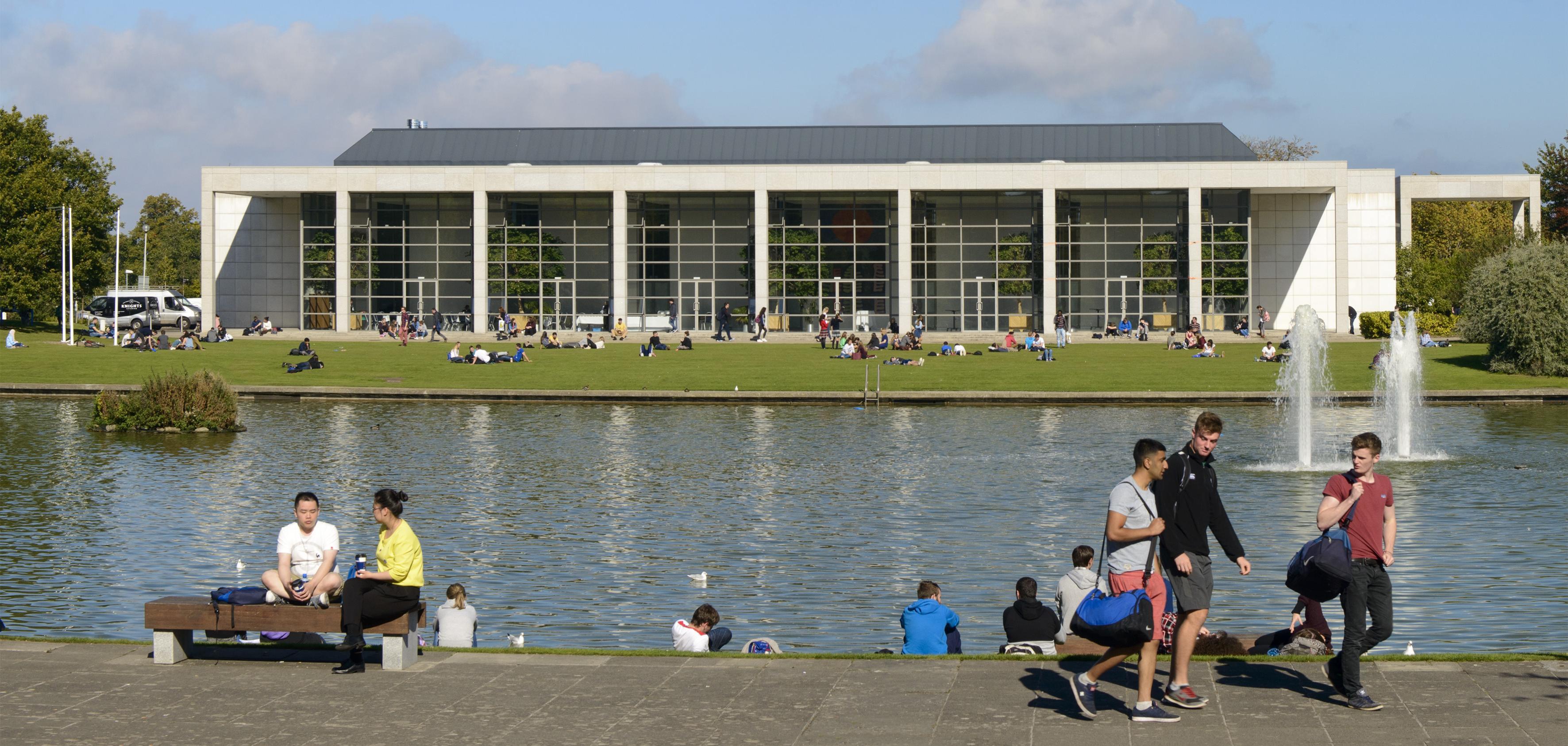 Students enjoying the sun in front of the main lake on UCD Belfield campus