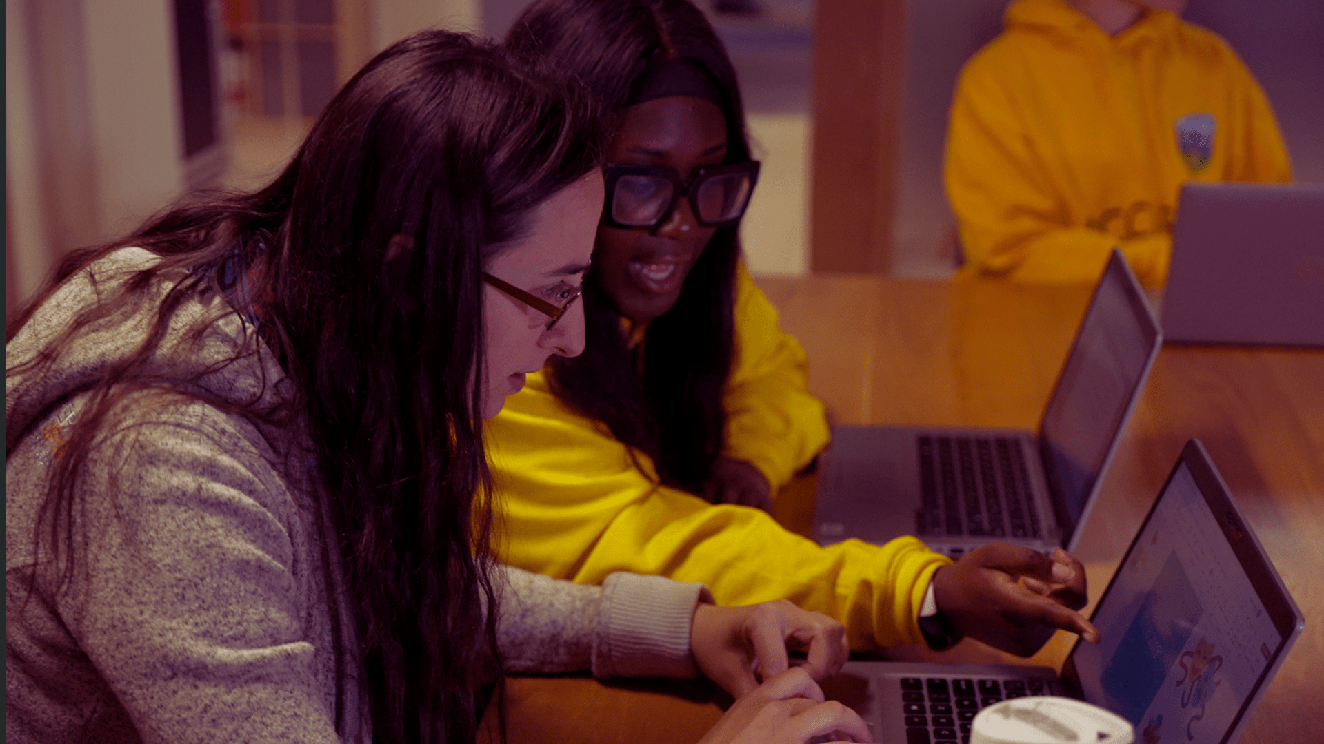Digital Ambassador in yellow hoodie assisting a person with a tech query at a laptop