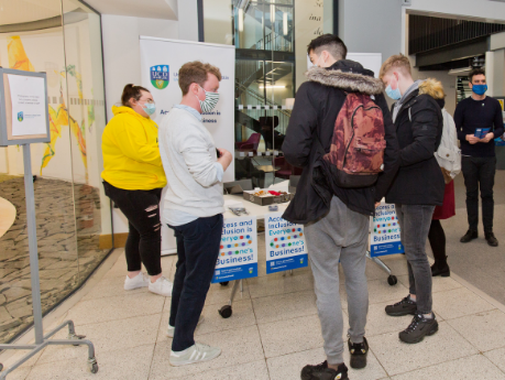 University for all stand on UCD campus - student access leader and UCD staff members chatting with students