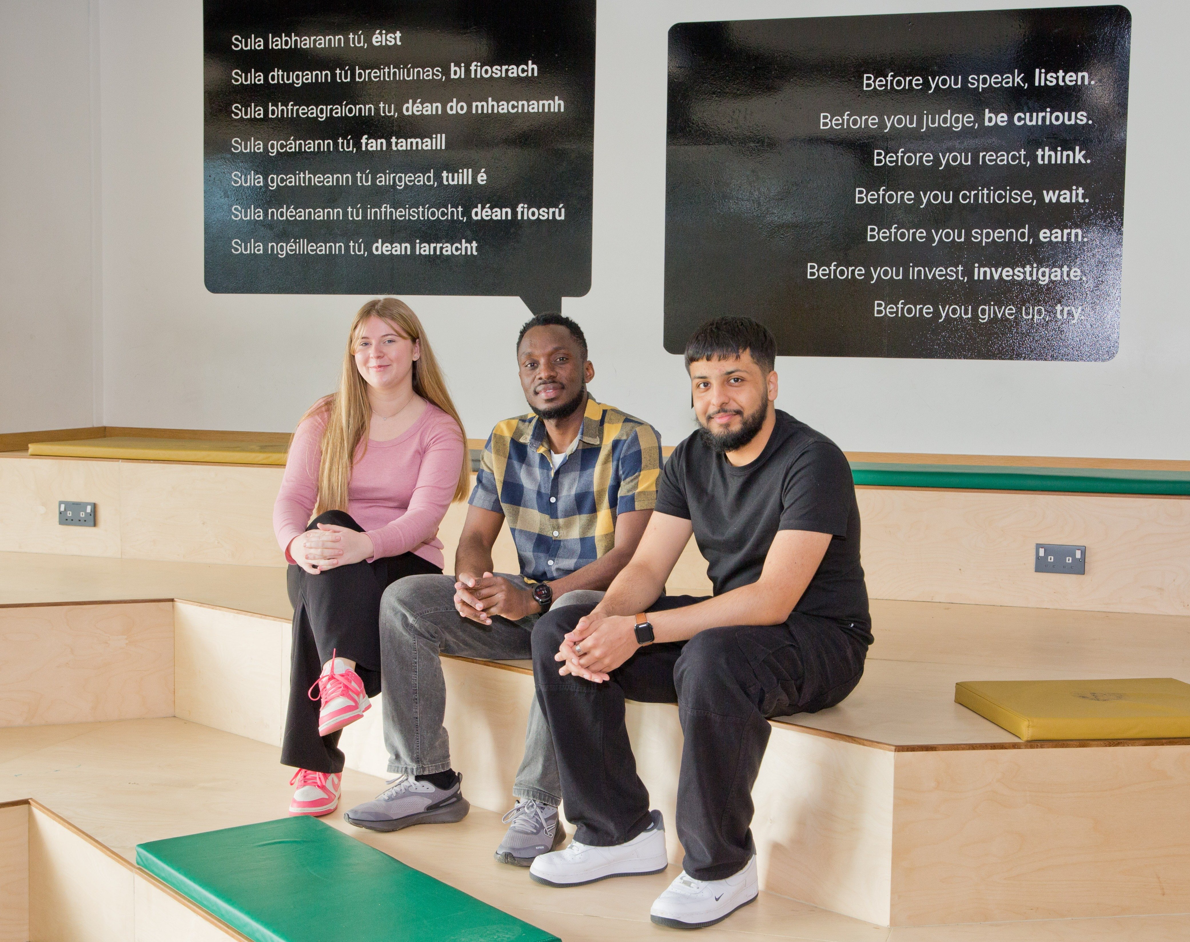 Three UCD students sitting on stairs, looking at the camera