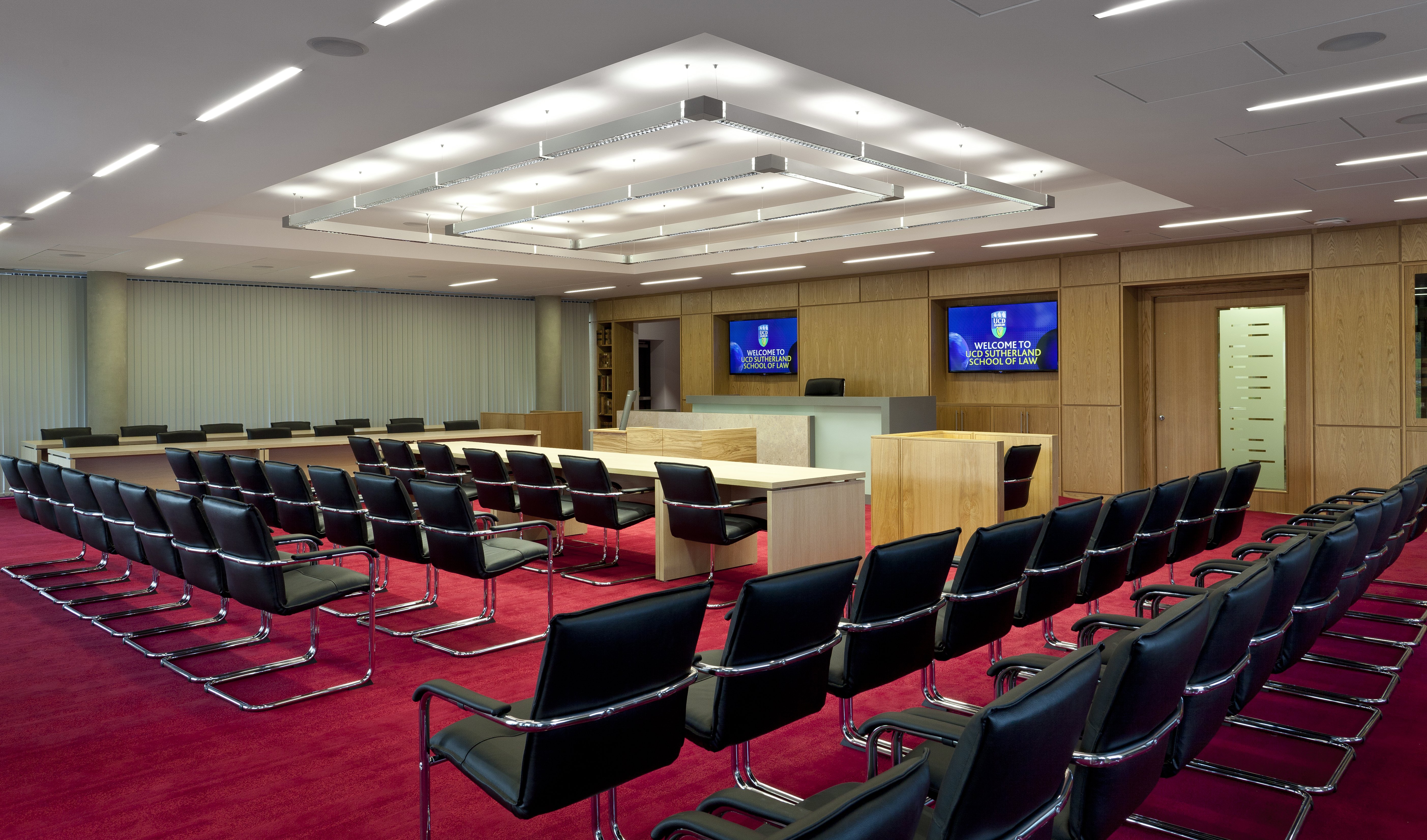 Rows of chairs facing the top of a room with screens behind a desk