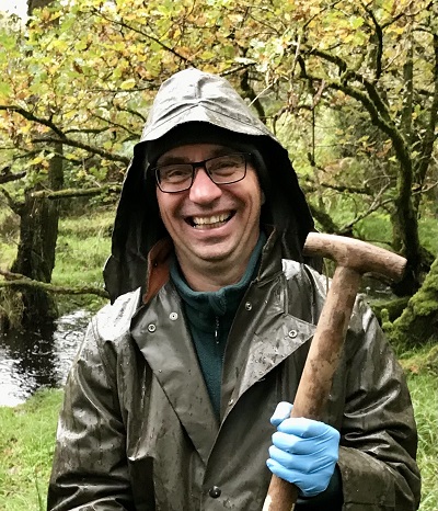 Professor Olaf Schmidt surrounded be trees in wet weather clothing holding a shovel