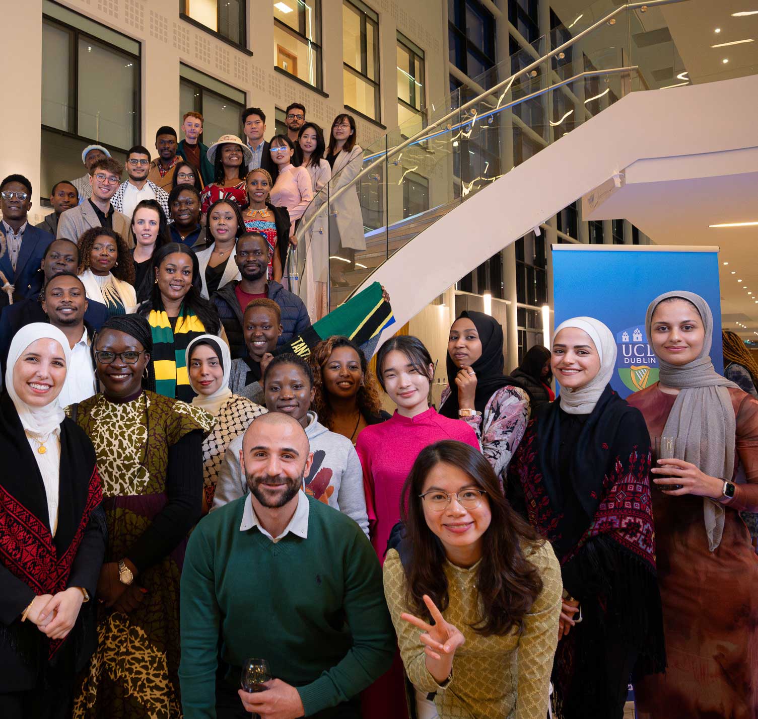 A large group of students smile to camera. The group stand both in front and alongside the staircase.