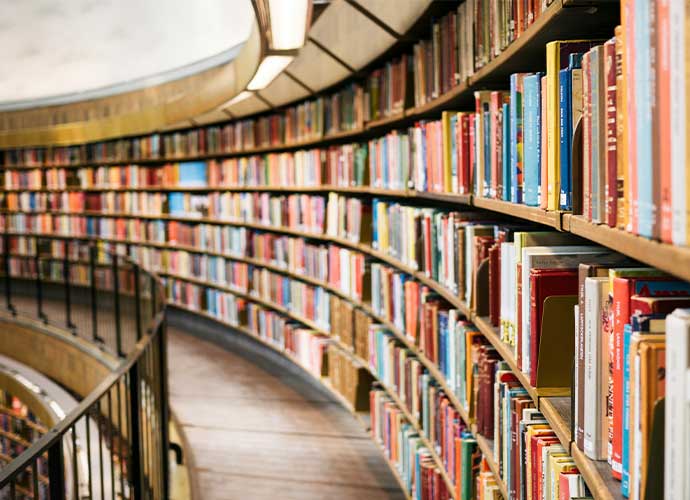 Curving library shelves packed with colorful books along a narrow walkway with a railing.