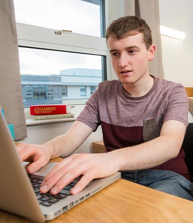 Male student typing on his laptop in UCD campus accommodation.