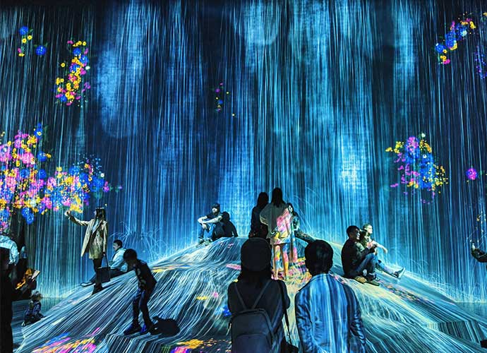 People interact with a digital art installation featuring cascading blue light projections and colorful flower-like visuals.