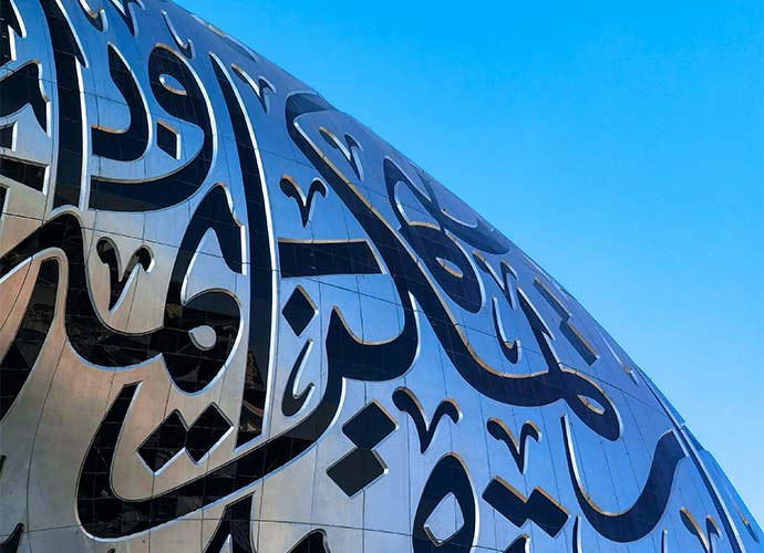 Close-up of the Museum of the Future in Dubai, showing reflective steel panels engraved with large Arabic calligraphy against a clear blue sky.
