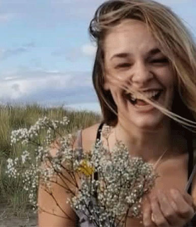 A young woman gives a big smile to camera while holding a bunch of delicate white flowers.