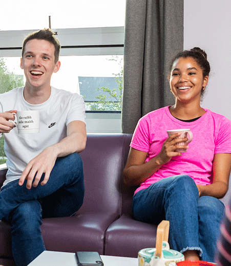 Two students sit on a sofa chatting over a hot drink.
