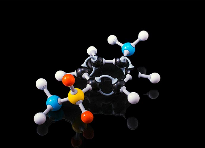 A colorful 3D molecular model with connected spheres representing atoms, displayed on a reflective black surface.