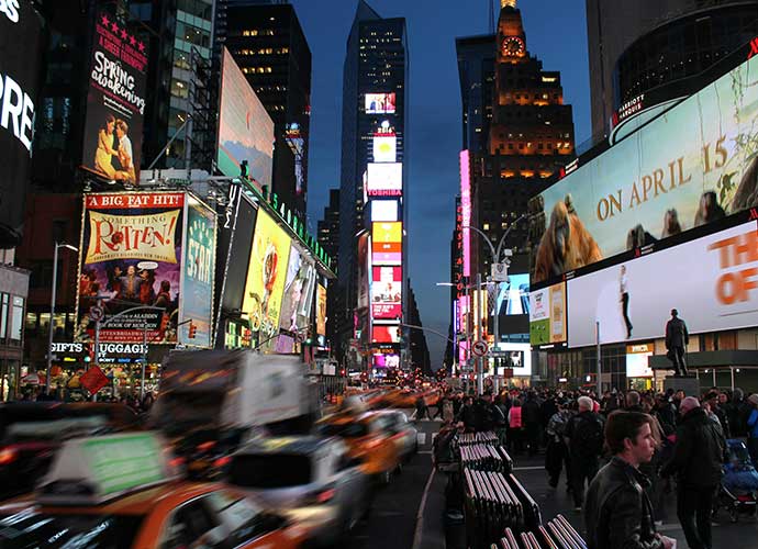 Busy Times Square in New York City at night, with crowds of people, taxis, and brightly lit billboards and advertisements covering tall buildings.