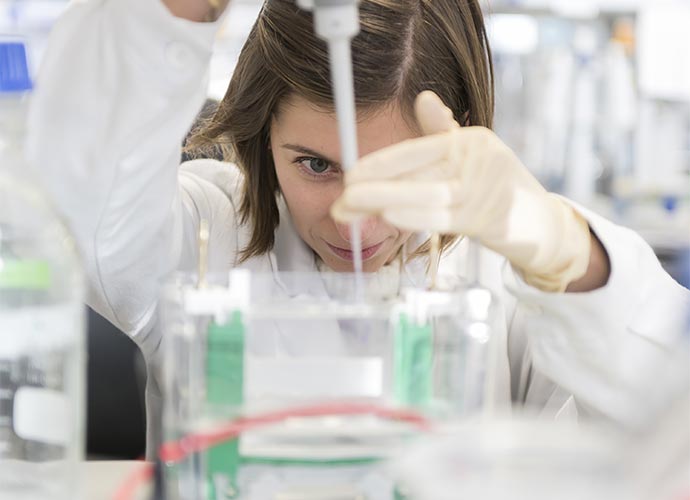 A scientist in a laboratory carefully pipetting liquid into a clear container, wearing a lab coat and protective gloves, focused on a precision experiment.