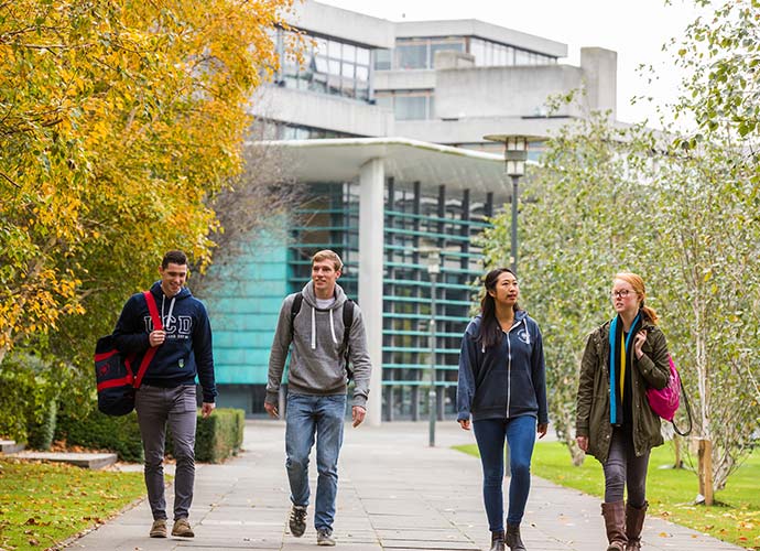 A group of four students walk along a path on UCD campus.