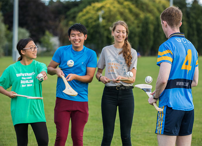 Four people standing on a grassy field practicing hurling.
