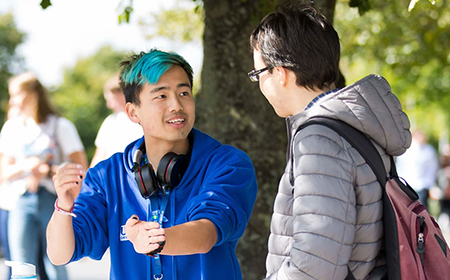 Young man with blue hair speaks to another man on the UCD campus.