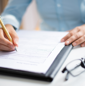 Person writing on a document, with glasses folded beside it