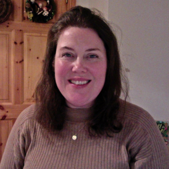 A headshot of a woman smiling with a white wall on the right side and wooden door on the left in the background