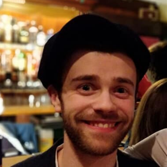 A headshot of a man smiling with blurred bar shelves in the background
