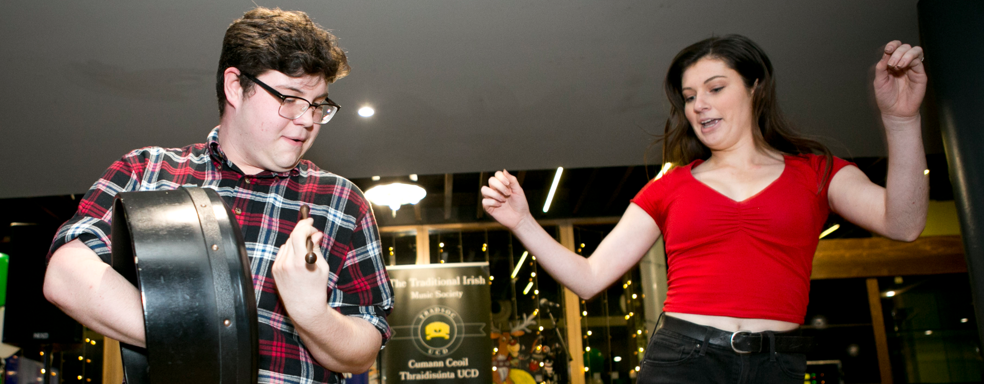 Two students in UCD Club House the student of the left playing the bodhran and the student on the right dancing