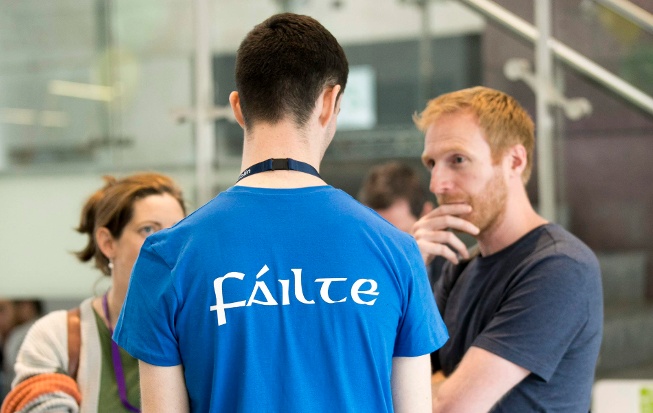 A picture of two men in conversation with one turned back to the camera wearing a t-shirt with