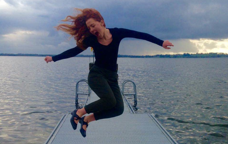 Girl jumping in mid air at a pier with sea in the background