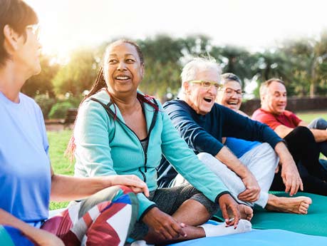 Group of people sitting in a park, laughing and taking part in exercise.