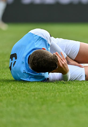 Young man in blue jersey lying on the ground on a pitch.