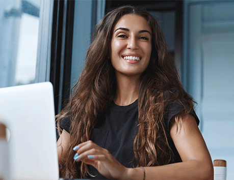 young woman with brunette hair smiling at laptop