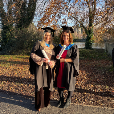Two UCD graduates in caps and gowns outside on a sunny day.