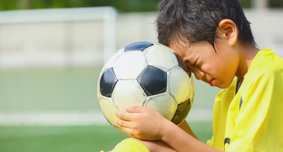 A boy holding a football looking sad