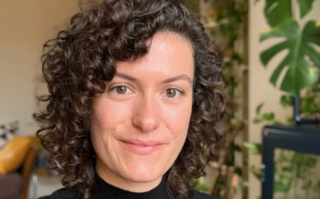 Woman with curly brown hair wearing a black top smiling to camera