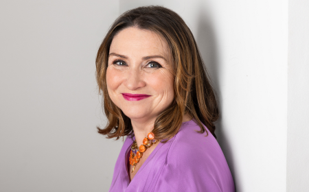 Woman with brown hair wearing a purple top smiling to camera