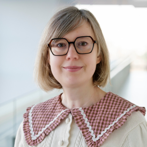 Woman with blonde hair wearing glasses and smiling to camera