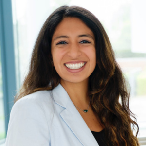 Woman with dark hair and white jacket smiling to camera