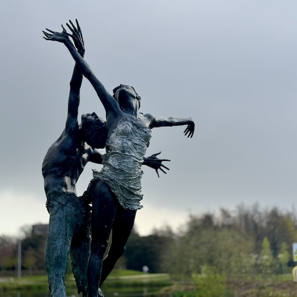 A statue of a pair of dancers framed against a grey sky and distant trees