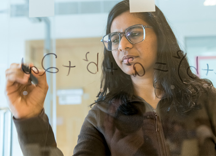 A postgraduate student writing an equation on a transparent screen
