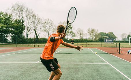 A man in an orange tee-shirt playing a tennis shot