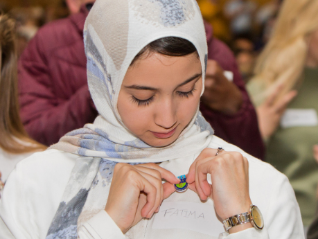 A new student placing a University for All pin on her lapel