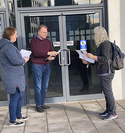 Photo of three members of the Vet School EDI team at the front door of the Vet Sciences Centre carrying notebooks and pens